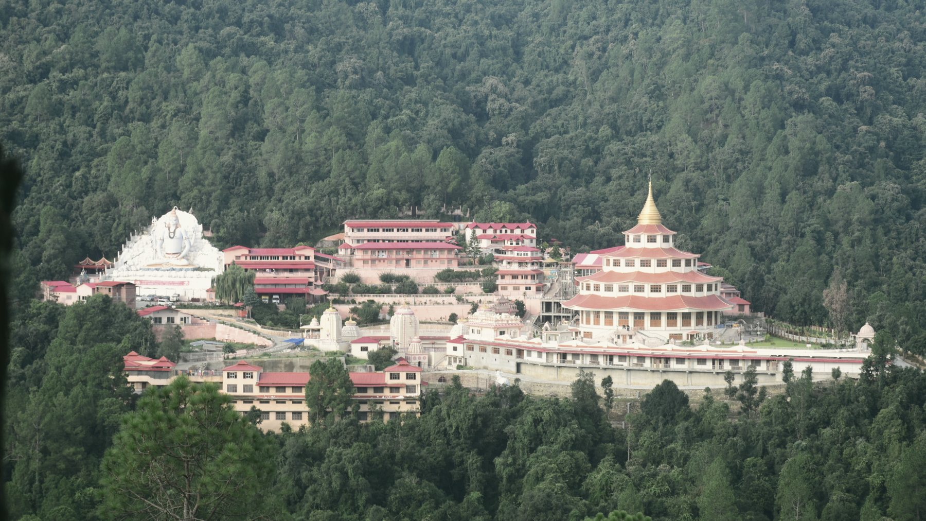 The Dol Ashram complex — its orange-roofed pagoda temple and grounds set into forested Kumaon hillside beneath the snow line